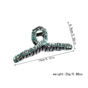 Detail view of large black hair claw clip decorated with teal rhinestones and white pearls.