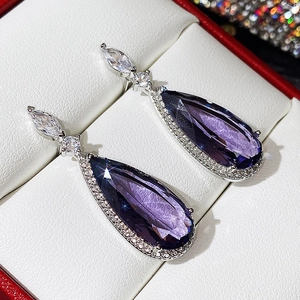 Détail macro de boucles d'oreilles goutte violettes sur support argenté en coffret