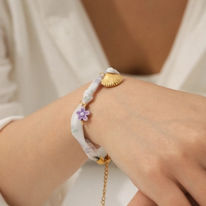 Detailed shot of stainless steel shell bracelet with purple floral silk fabric and golden charms