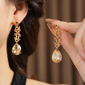 Detailed close-up of a long teardrop champagne crystal earring in a gold finish setting
