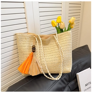 Detail of straw woven tote bag with fringe charm and braided handles on a leather sofa