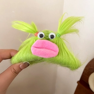 Close-up of green plush monster hair claw with pink lips and funny googly eyes