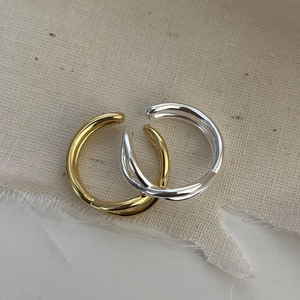 Close-up of minimalist gold and silver crossover rings on textured beige fabric