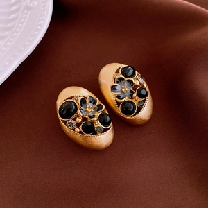Detail of vintage enamel flower earrings with black stones and brushed gold finish