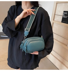 Detail of dark green crossbody camera bag featuring lychee texture and striped strap