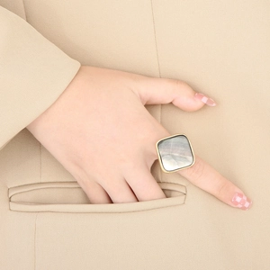 Detail of square gold stainless steel shell ring worn on hand with tan blazer pocket