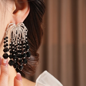 Close-up of black glass bead tassel earrings with silver finish on a model's ear