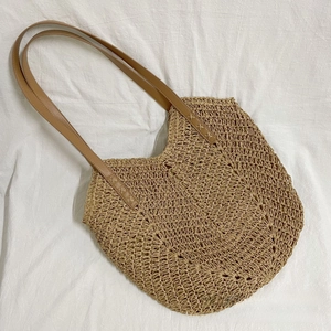 Detail of hollow hand-woven straw tote with premium brown faux leather shoulder strap