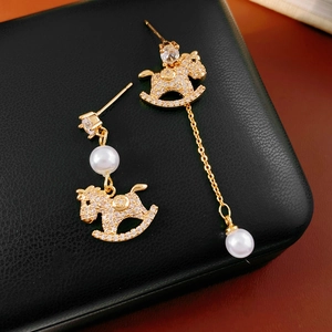 Macro shot of gold-plated rocking horse earrings with pearls and zircon on black leather