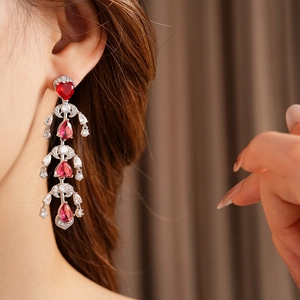 Close-up of red heart-shaped drop earrings with silver fringe on model's ear