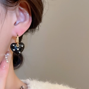 Close-up of heart-shaped earring with small diamonds worn on ear with golden clasp