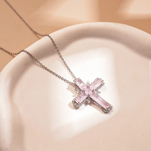 Gros plan détaillé d'un pendentif croix argenté avec gemmes roses et cristaux micro-pavé