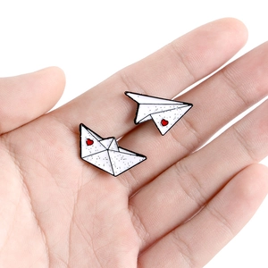 Pair of enamel pins featuring paper plane and boat shapes with red heart accents