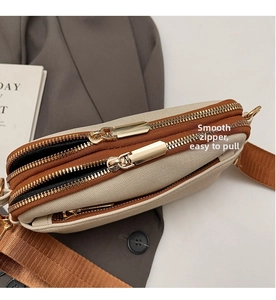 Detailed close-up of smooth gold zippers on a beige canvas crossbody bag with brown trim