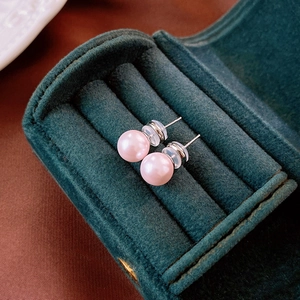 Macro shot of pink pearl earrings with silver posts inside a dark green velvet jewelry box
