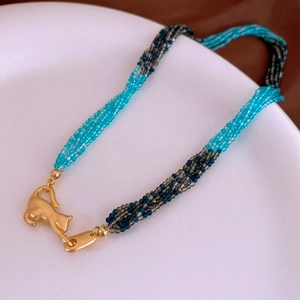Detail of multi-strand beaded necklace with a golden cat pendant on a white ceramic plate