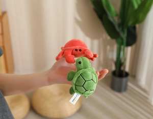 Close-up of plush red crab and green turtle animal pendants held in hand for size