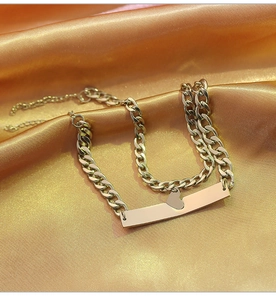Detail of a gold curb chain bracelet featuring a polished heart and square plate design