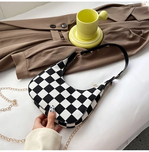 Detail of checkerboard crescent bag with gold chain strap on a blazer background