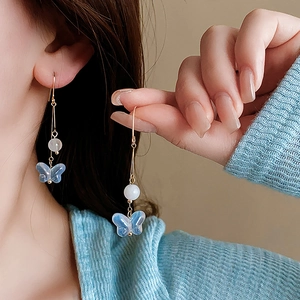 Detail of blue butterfly tassel earrings with golden hooks and white beads on a model