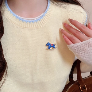 Detail of blue rocking horse brooch with gold plating and rhinestones on beige sweater