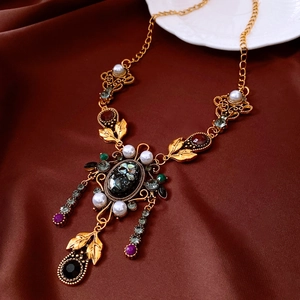 Dettaglio di una collana vintage dorata con pietre colorate, perle bianche e nappe eleganti