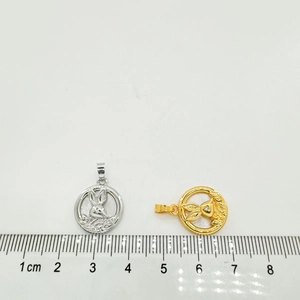 Detail view of gold and silver shell rabbit pendants next to a ruler for size reference