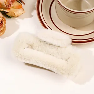 Detailed close-up of cream fuzzy plush claw clip on a table with vintage floral accents