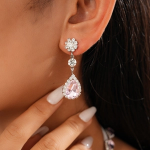Macro view of pink teardrop gemstone earrings with white zircon accents on a model