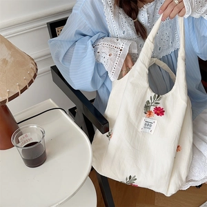Close-up of floral embroidery and woven label on a cream canvas tote bag detail