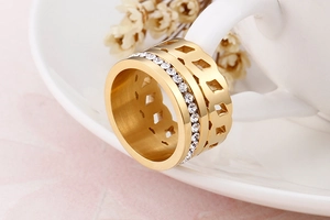 Dettaglio di un anello largo dorato con zirconi bianchi e texture a catena cava