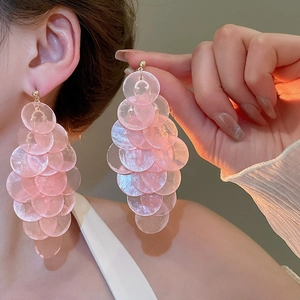 Detailed shot of pink beaded shell tassel earrings worn by a model in warm light