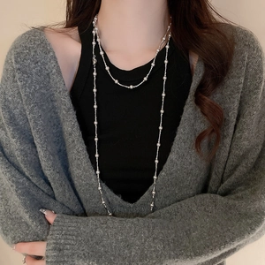 Détail d'un long collier à billes argentées porté en double rang sur un pull gris chic