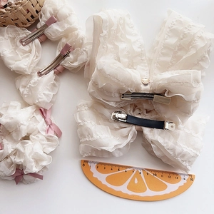 Detail of ruffled beige chiffon bow hair clip and matching scrunchie with layered texture