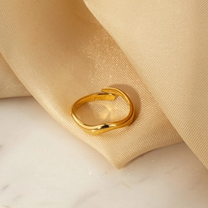 Macro detail of adjustable gold wave ring on luxurious beige silk and marble background