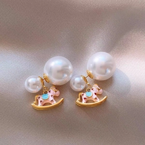 Detailed close-up of a pink enamel rocking horse earring with gold pearl accents
