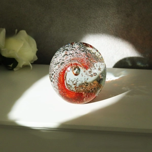 Detail of handmade crystal paperweight with red spiral pattern and gold glitter flakes