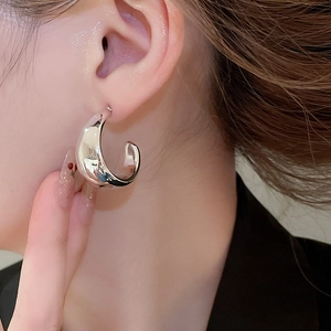 Close-up of polished silver C-shaped chunky hoop earring on model showing sleek metallic shine