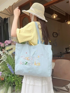 Sac cabas en toile bleu clair avec broderie Lucky Zakka présenté en extérieur décontracté