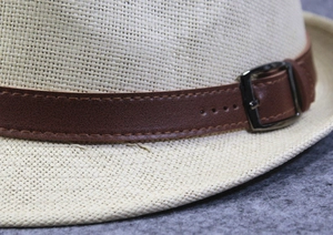 Close-up of beige woven straw hat with brown leather band and metal buckle detail