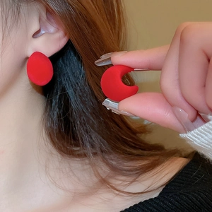 Close-up of stylish red flocked C-shaped earrings with a soft matte texture on a model