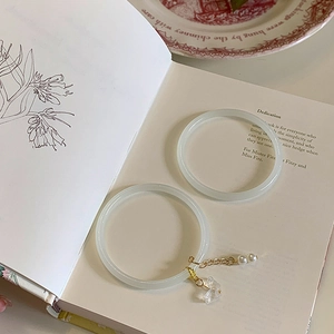 Detail of two translucent bangles with gold chain, pearl, and butterfly charm on a book