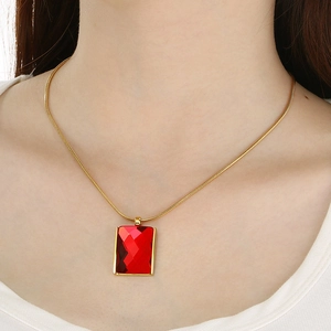 Close-up of a gold snake chain necklace with a large square red glass pendant on model