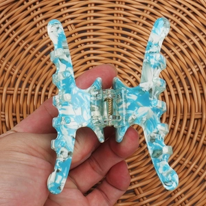 Detail of blue marbled acetate hair claw clip with gold spring on woven background