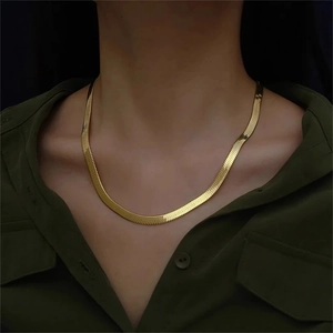 Close-up of a flat gold snake bone chain necklace worn by a model on a dark background