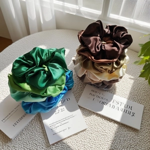 Detailed view of assorted satin silk scrunchies in green blue and earthy brown tones