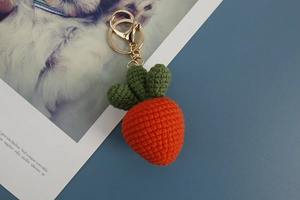 Detailed close-up of a handmade knitted carrot keychain with orange yarn and green leaves