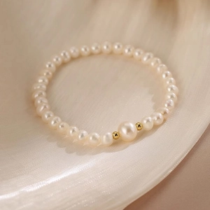 Detail of freshwater pearl bracelet with gold spacers on soft white silk background