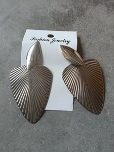 Macro shot of oversized silver leaf earrings with detailed fan texture on grey background