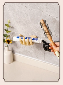 Hand-shaped adhesive wall hooks holding toothpaste and a hairbrush on a marble wall